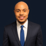 A stunning young black marketing professional in a black suit with blue neck tie.